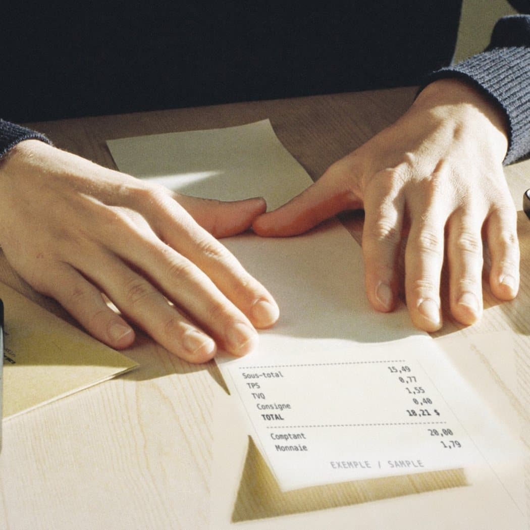 Two hands smoothing a receipt flat on a kitchen table before taking its photo.
